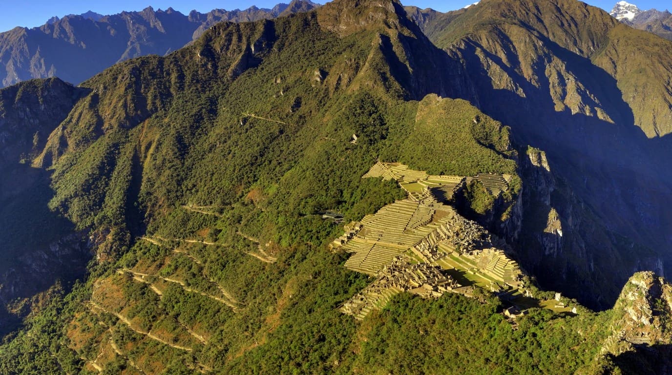 Hiker standing at the summit of Huayna Picchu looking down at the ancient Machu Picchu citadel ruins in Cusco, Peru