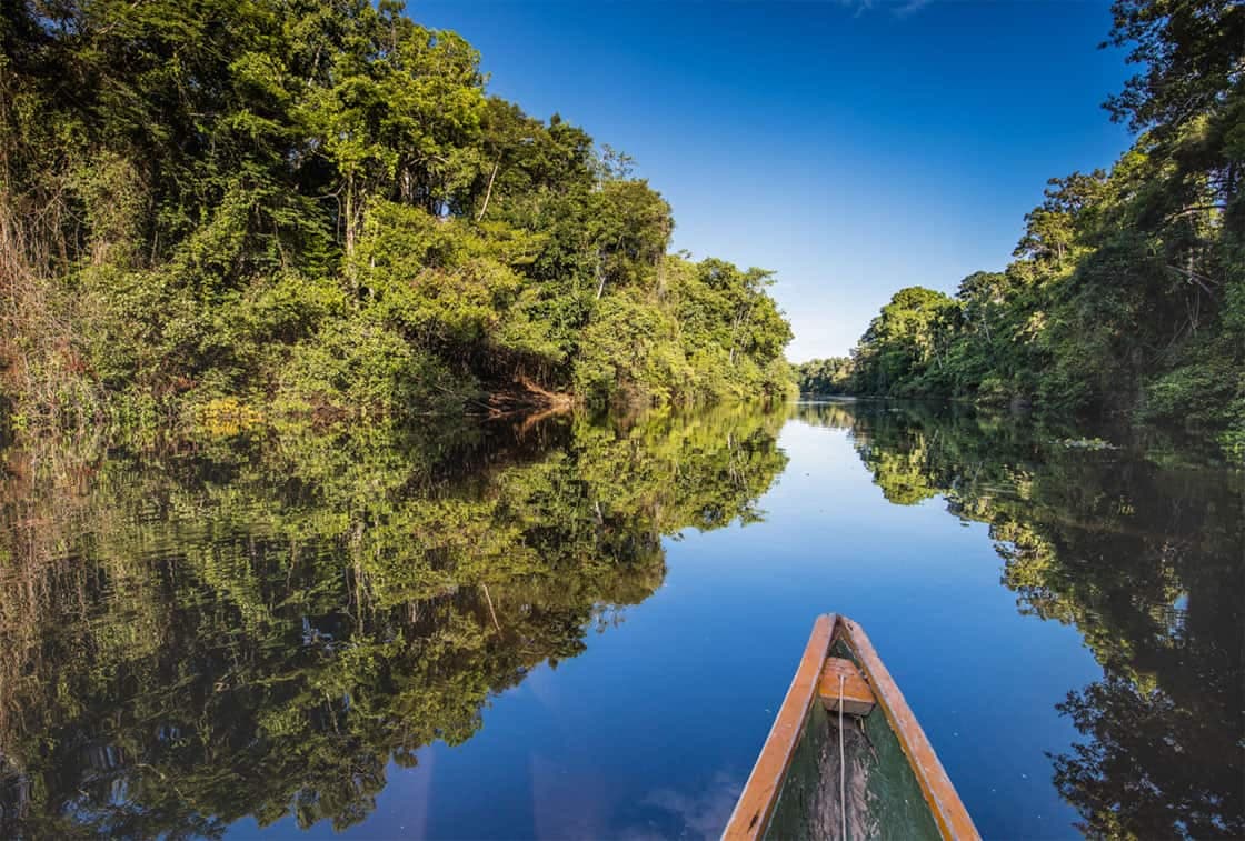 Expedition canoe navigating tranquil mirror waters in Pacaya Samiria National Reserve near Iquitos